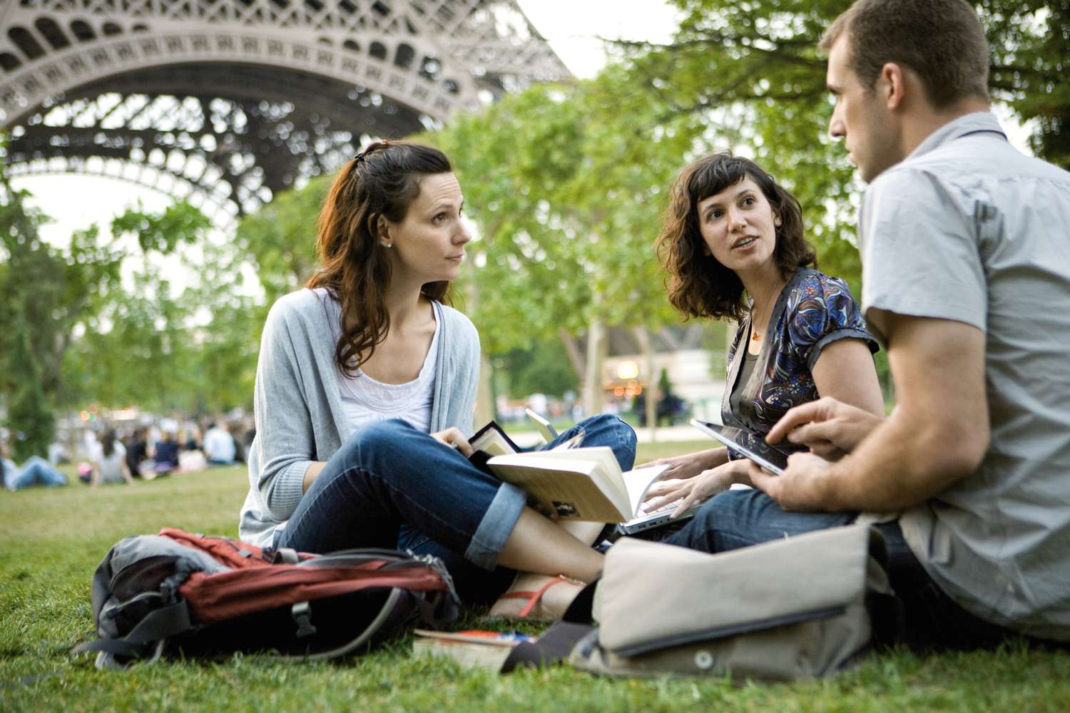 Three students studying and conversing on the grass near the Eiffel Tower